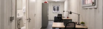 Interior of an office container with workstations and an integrated toilet compartment for temporary site use.