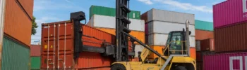 Reach stacker handling a dry shipping container at a depot, illustrating handling and logistics costs for European buyers.