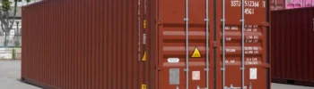 Red shipping container at a depot, with its doors, locking bars and identification markings clearly visible.