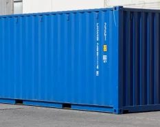 Blue shipping container at a depot, with its identification number and size/type markings visible on the side panel.