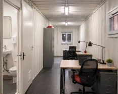 Interior of an office container with workstations and an integrated toilet compartment for temporary site use.
