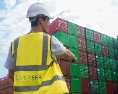 SILVERSEA Containers worker wearing a hard hat and high-visibility vest, pointing towards stacked shipping containers at a depot.