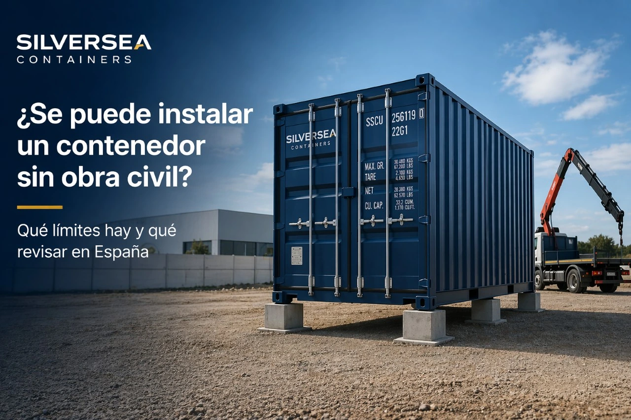 Contenedor marítimo Dry Van instalado sobre apoyos ligeros en una parcela industrial en España, sin losa visible, con camión grúa al fondo.