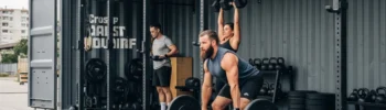 Gimnasio modular de alto rendimiento y box de CrossFit construido en un contenedor marítimo High Cube, abierto en un lateral para entrenamiento al aire libre. La imagen muestra el suelo de caucho anti-impacto y estructuras de dominadas (Rigs) fijadas a la estructura de acero Corten