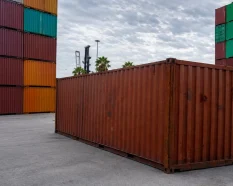 Contenedor marítimo usado en un depósito exterior bajo un cielo nublado, expuesto a cambios de humedad y temperatura.